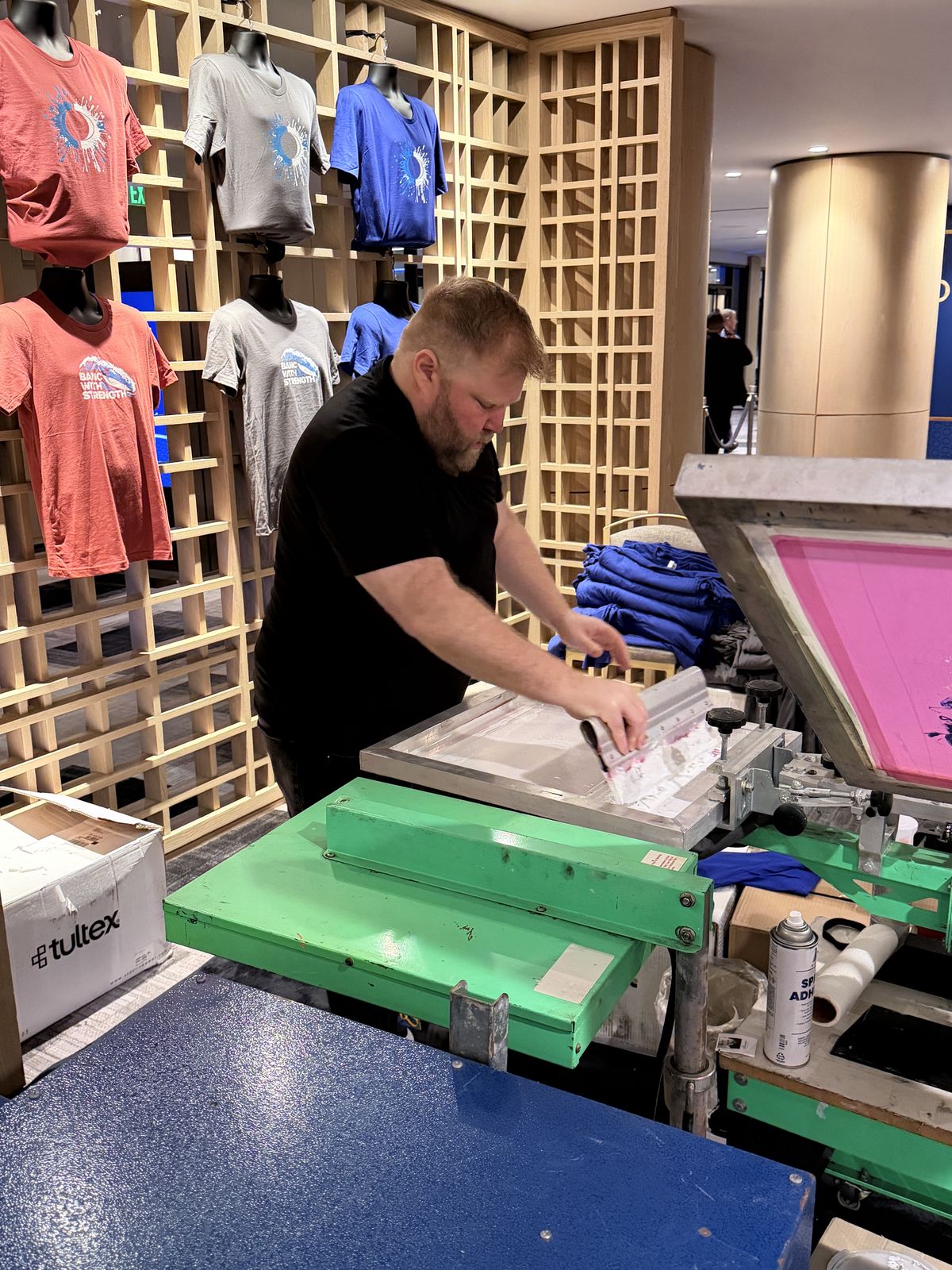 Merch Troop operator running a live personalization station beside a wall of finished garments